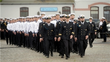 Rekrutinnen und Rekruten der der Marineoperationsschule Bremerhaven: Frauen und Männer in mal weißen oder dunkelblauen Marine-Uniformen marschieren einen Weg entlang.