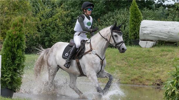 Eine Person auf einem weißen Pferd läuft durch Wasser.