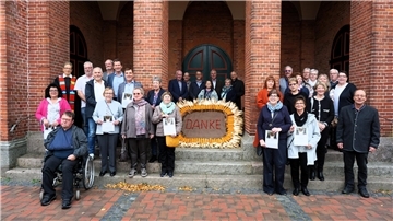 Gruppenfoto von 32 Jubilarinnen und Jubilaren der Goldenen Konfirmation vor der Fabian- und Sebastian-Kirche in Beverstedt. Die Teilnehmenden stehen auf den Treppen vor dem Eingang, in der Mitte ist ein großes Erntedankbild mit der Aufschrift „DANKE“ platziert.