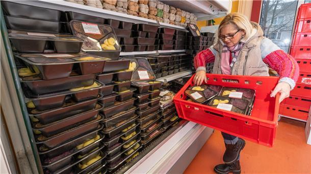 Eine Frau hält eine Kiste mit verpackten Essen und räumt diese in ein Regal.