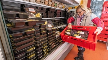 Eine Frau hält eine Kiste mit verpackten Essen und räumt diese in ein Regal.