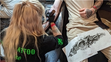 Eine Tätowiererin aus den Niederlanden sticht ein Tattoo auf einen Arm eines Besuchers.