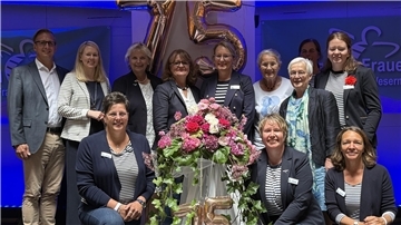 Mehrere Menschen stehen mit Blumen vor einer goldenen 75. 