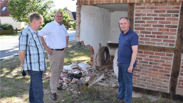 Und wieder kracht es in tückischer Rhader Unfallkurve Abermals ist die Garage an der Selsinger Straße in Ostrhade beschädigt: Bürgermeister Marco Mohrmann (Mitte), sein Stellvertreter Thomas Brunckhorst (links) und Rüdiger Meyer vom „Hof Stoffers“ an der Unfallstelle.