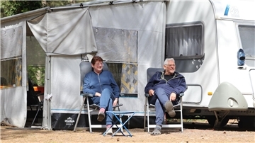 Ein Ehepaar sitzt vor einem Campingwagen. Alles andere als Neuling sind Marta und Uwe Baars. Sie campen seit 40 Jahren und wissen, was beim Campingurlaub nicht fehlen darf.