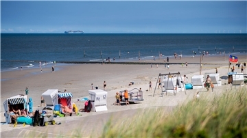 Touristen sitzen bei sonnigem Wetter in Strandkörben am Strand