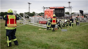 Feuerwehrleute mit umgekippten Bühnenaufbauten auf dem Festivalgelände
