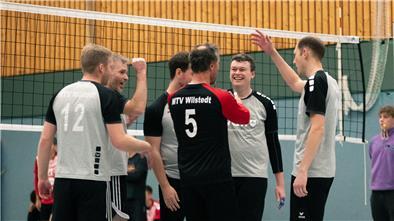 Männer stehen vor einem Volleyballnetz und jubeln. 