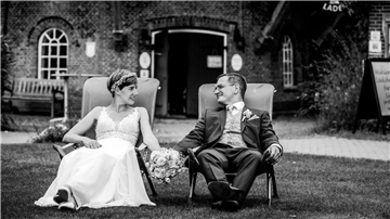 Hochzeitspaar sitzt nebeneinander auf Stühlen auf dem Rasen