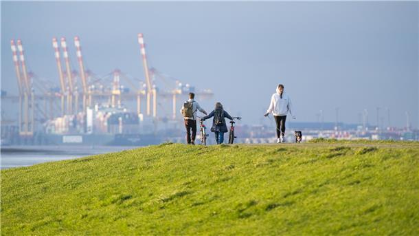 Der perfekte Tag in Bremerhaven für Sie und Ihren Hund Eine Person mit Hund und zwei Radfahrer genießen die Aussicht am Lunedeich in Bremerhaven.
