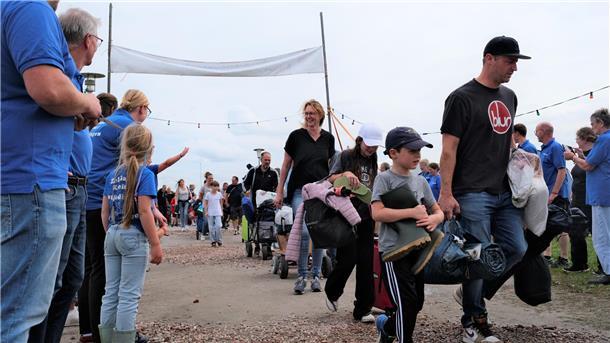 Zeltlager in Burhave: Über 100 Kinder machen diesmal mit Dutzende bepackte Kinder und ihre Eltern laufen einen Weg entlang. Am Rand stehen Menschen in blauen T-Shirts.
