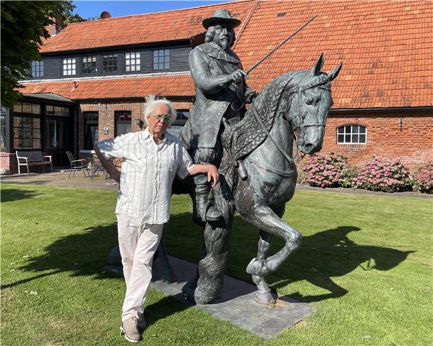 Mann steht neben lebensgroßer Bronzeskulptur eines Reiters.