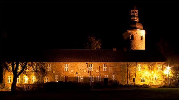 Zeven macht das Licht aus: Earth Hour 2025 für Klimaschutz Ein langgestrecktes Gebäude und ein Kirchturm werden in der Dunkelheit angestrahlt.