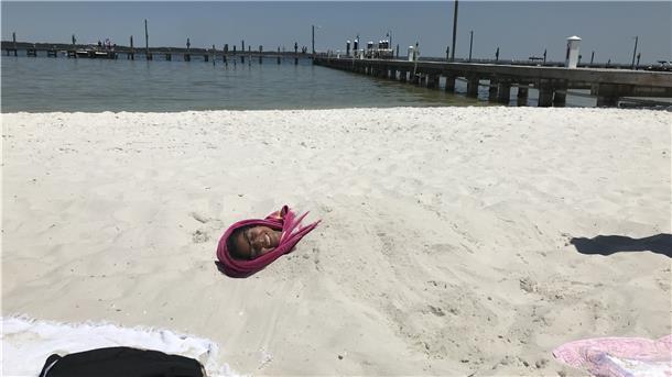 Eine Frau liegt verbuddelt am Strand von Santa Rosa Sound Beach.