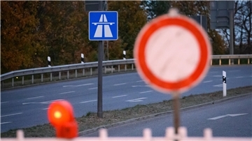 Ein Stoppschild steht im Hintergrund, ein Autobahn-Hinweisschild im Hintergrund.
