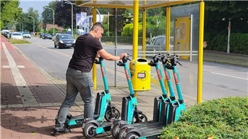 Ein Mann stellt E-Scooter an einer Bushaltestelle auf. 