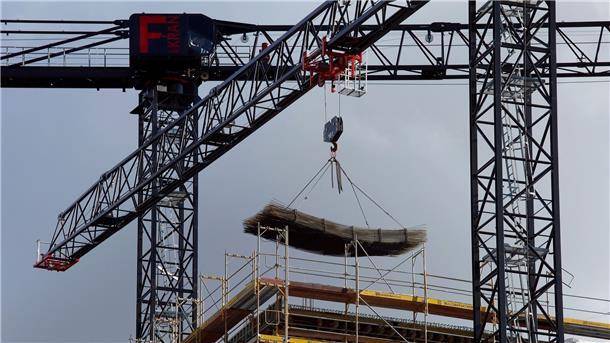 An einem Baukran wird Baumaterial auf einer Baustelle des Quartiers Heidestraße in Berlin transportiert.