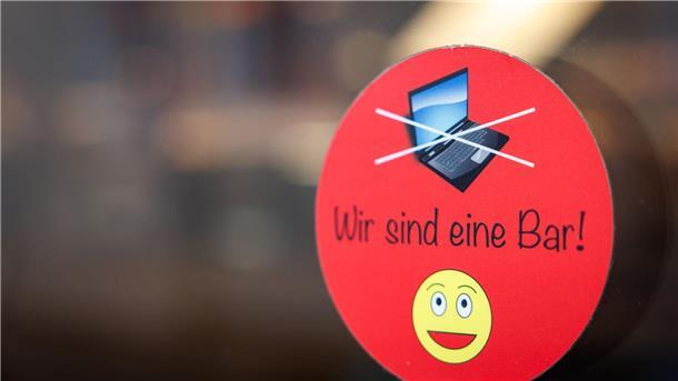 Warum Cafés Laptops verbannen An einer Scheibe der Café-Bar 8tto Grammi in Bayreuth weist ein Schild auf das Verbot von Laptops hin.