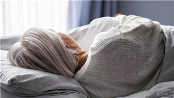 Eine Seniorin mit grauen Haaren liegt auf einem Bett.