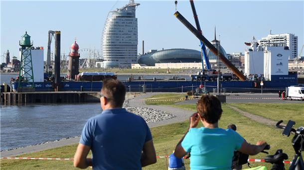 Rückblick auf das Drama um den schiefen Molenturm: Kippt er oder kippt er nicht? An Tag drei der Havarie, am 20. August 2022, geht der schwerlastfähige Ponton „BHV Innovation“ in der Geesteeinfahrt in Stellung. Er ist die Arbeitsbühne, auf der auch 110 Strohquader gestapelt werden, auf die der Turm fallen könnte. Jetzt versuchen die Fachleute der Bergungsfirma zu retten, was noch zu retten ist: Der Turm soll so abgetragen werden, dass später möglichst viele Teile für den Wiederaufbau wieder verwendet werden können.