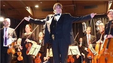 Ein Mann im Smoking vor Männer und Frauen mit Streichinstrumenten.