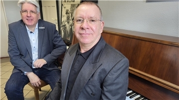 Zwei Männer in Jackett sitzen an einem Klavier. Die LzO hat dem Leiter der Jahnhalle Nordenham einen Geldscheck über 2.500 Euro überreicht. 