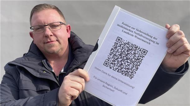 Ein Mann hält eine Mappe in den Händen, auf deren Deckblatt ein QR-Code zu sehen ist.