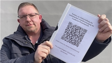 Ein Mann hält eine Mappe in den Händen, auf deren Deckblatt ein QR-Code zu sehen ist.