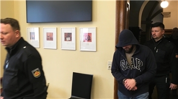 Ein Mann betritt den Raum, begleitet von Polizeibeamten.
