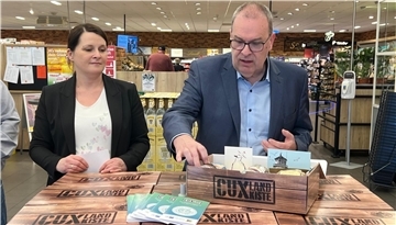 Ein Mann und eine Frau präsentieren in einem Supermarkt die CuxlandKiste mit regionalen Produkten. Sie stehen vor einem Stapel von Kisten, eine Kiste ist geöffnet. Daneben liegen einige Flyer.