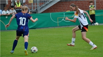 Zwei Mädchen spielen auf einem Rasen mit einem Fußball.