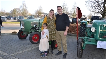 Eine Frau und ein Mann stehen mit ihrer kleinen Tochter vor einem historischen Schlepper.