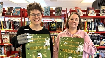 Zwei Frauen halten Plakate hoch, die auf einen Halloween-Abend hinweisen.