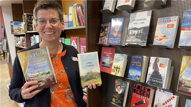 Eine Frau vor einem Bücherregal mit zwei Büchern in der Hand
