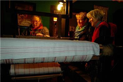 Annelene Lühmann-Jesewski steht am Webstuhl und erklärt die Arbeitsschritte beim Weben.