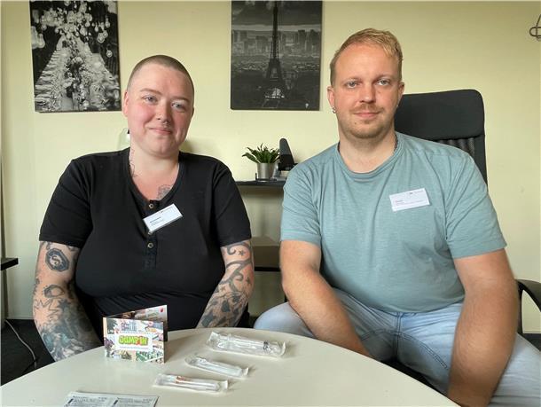 Eine Frau und ein Mann. Sie sitzen an einem Tisch, auf dem Spritzen bzw. Nadeln liegen.