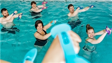 Männer und Frauen stehen im Wasser und heben die Arme.