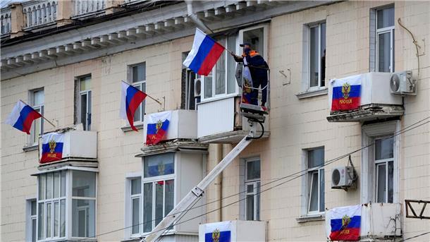 Arbeiter hängen russische Fahnen an einem Wohnhaus in der von Russland unterstützten und von Separatisten kontrollierten Volksrepublik Luhansk auf.