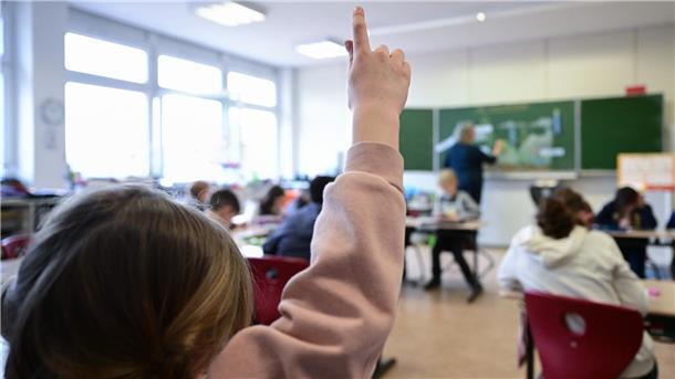 Ein Mädchen hebt im Unterricht in einer Schule den Finger.
