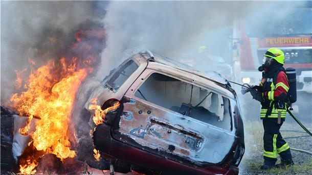Ein brennendes Auto wird von einem Feuerwehrmann gelöscht