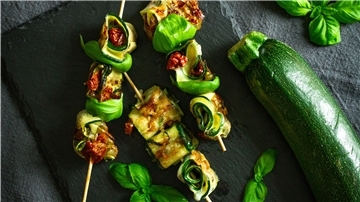 Auch lecker für die Grillparty: Zucchinischeiben werden mit Mozarella und getrockneten Tomaten belegt, dann aufgerollt und schließlich auf Holzspießchen fixiert.
