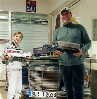 Auch Mike de Buhrs Sohn Josh begeistert sich für Modellautos. Dieses „Ghostbuster“-Auto aus Legosteinen hat er selbst zusammengebaut. Sein Vater hält einen historischen Lastwagen der Bundesbahn in Händen.