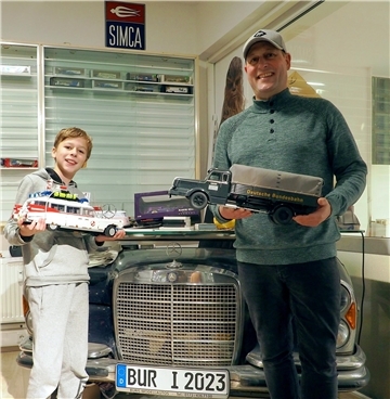Auch Mike de Buhrs Sohn Josh begeistert sich für Modellautos. Dieses „Ghostbuster“-Auto aus Legosteinen hat er selbst zusammengebaut. Sein Vater hält einen historischen Lastwagen der Bundesbahn in Händen.
