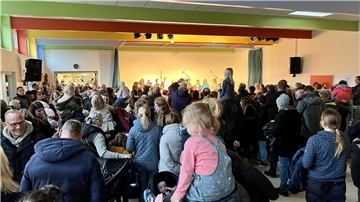 Kinder und Erwachsene haben sich in der Pausenhalle versammelt. 