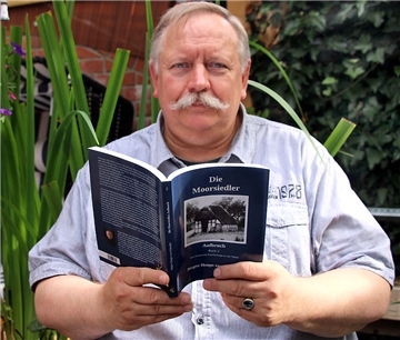 Jürgen Hoops hält sein Buch in den Händen und schaut in die Kamera.