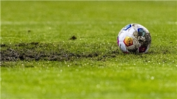 Ein Fußball liegt am Elfmeterpunkt im matschigen Rasen.