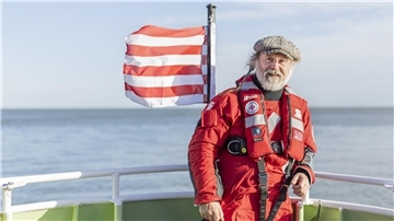 Autor Klaus-Peter Wolf auf einem Schiff. Im Hintergrund weht eine rot-weiß gestreifte Flagge.