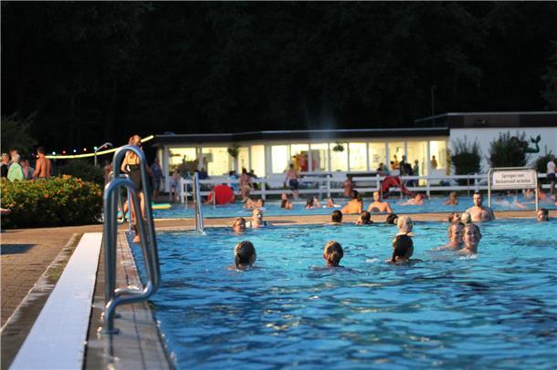 Menschen schwimmen unter Flutlicht. Das Flutlichtbaden ist die Hauptattraktion in Hepstedt.