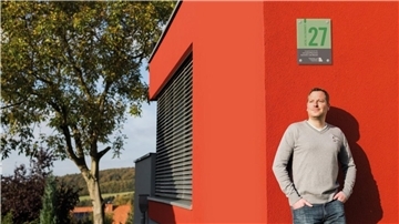 Mann lehnt entspannt an einer orangen Hauswand