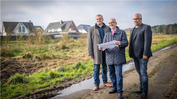 Bauunternehmer Anatoli Delgas (links) von EG Massivhausbau, Baustadtrat Bernd Schomaker (Mitte) und Finanzierungsberater Andre Wittmann stehen vor dem zu erschließenden Bauland am Plätternweg.
